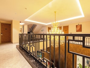 A hotel lobby with a modern chandelier, a wooden reception desk, and a staircase.