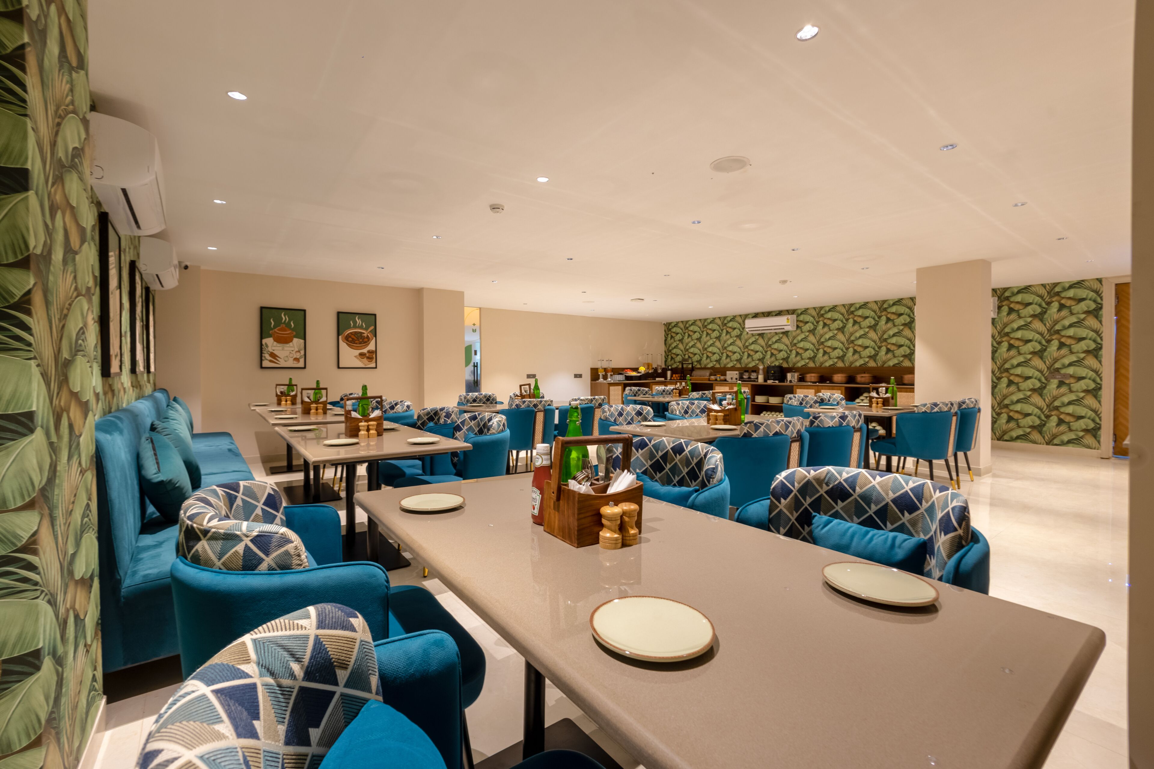 A spacious dining area with multiple tables and blue upholstered chairs, featuring a neutral color palette and tropical wallpaper.