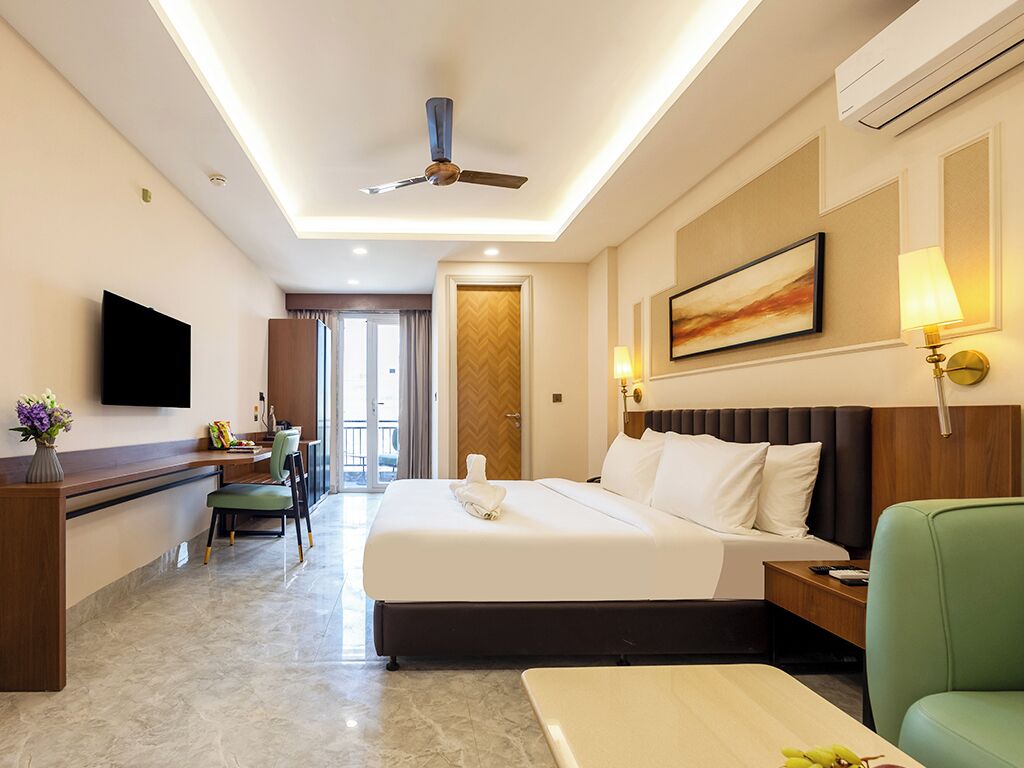 A hotel room with a bed, a desk, a chair, a television, and a ceiling fan.