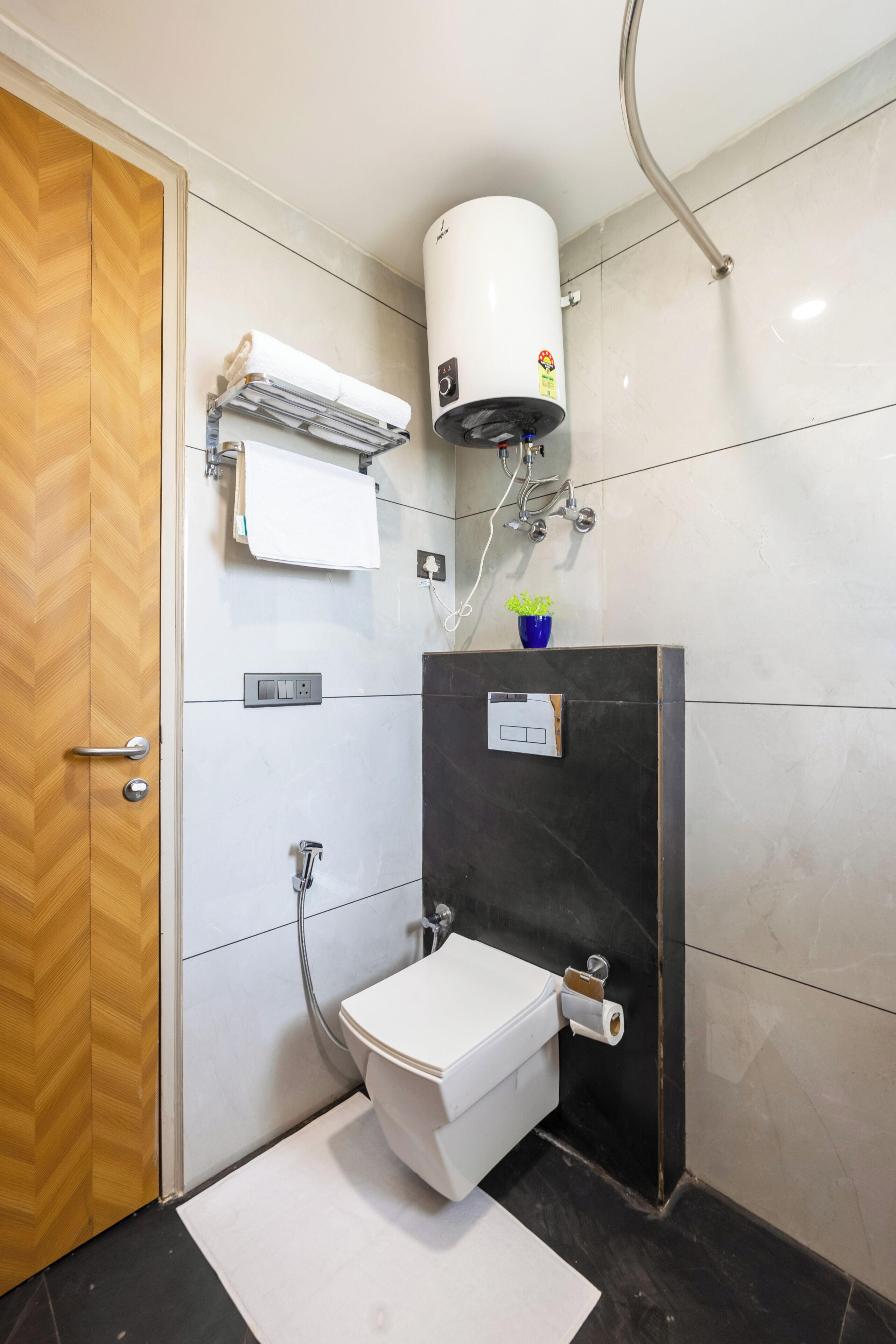 A modern bathroom with a toilet, a towel rack, a heater, and a small plant on the sink.