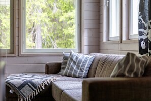 Une pièce chaleureuse avec un coin salon confortable, une fenêtre donnant sur les arbres et un plaid à motifs.
