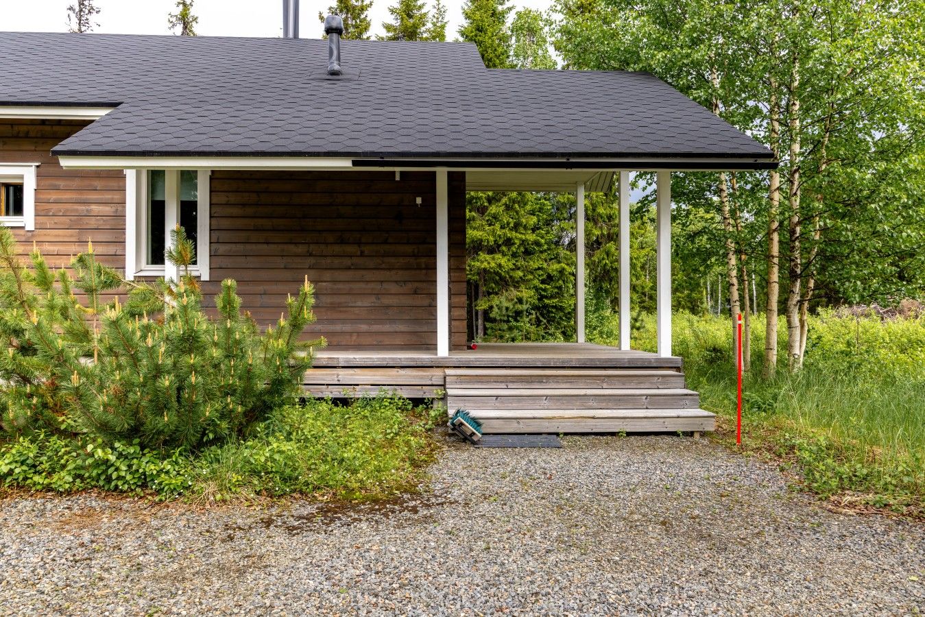 A modern house with a wooden exterior, a covered porch, and a gravel driveway.