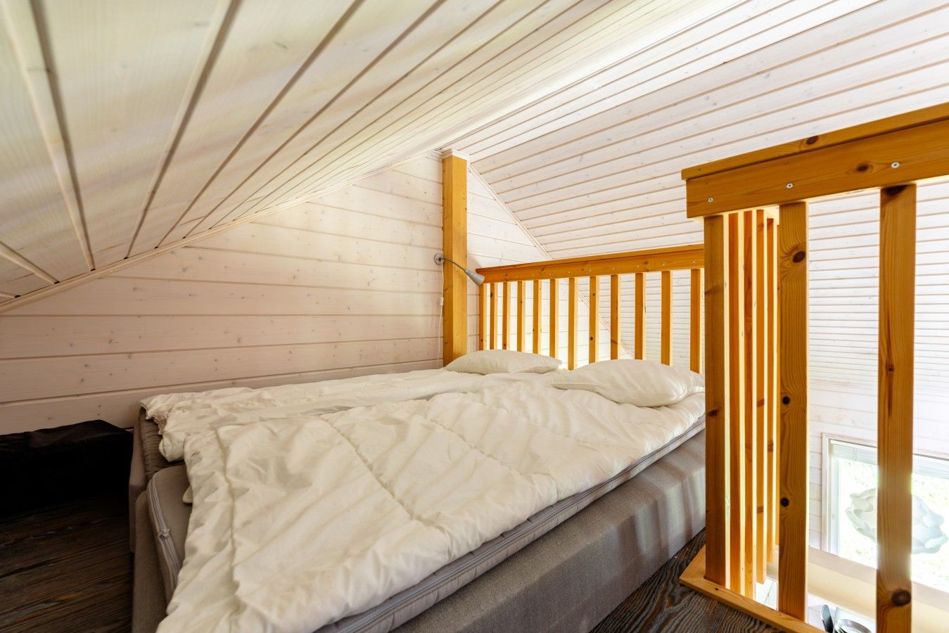 A single bed in a cabin with a sloped ceiling and wooden beams.
