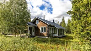 Une cabane en bois dotée d’un porche, entourée d’une forêt dense.