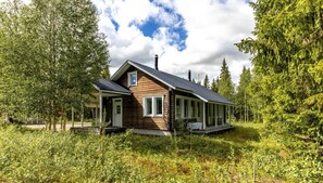 Une cabane en bois dotée d’un porche, entourée d’une forêt dense.