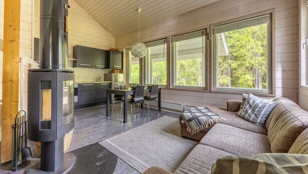 Un intérieur de chalet chaleureux avec un poêle à bois, un coin repas, un canapé et de grandes fenêtres.