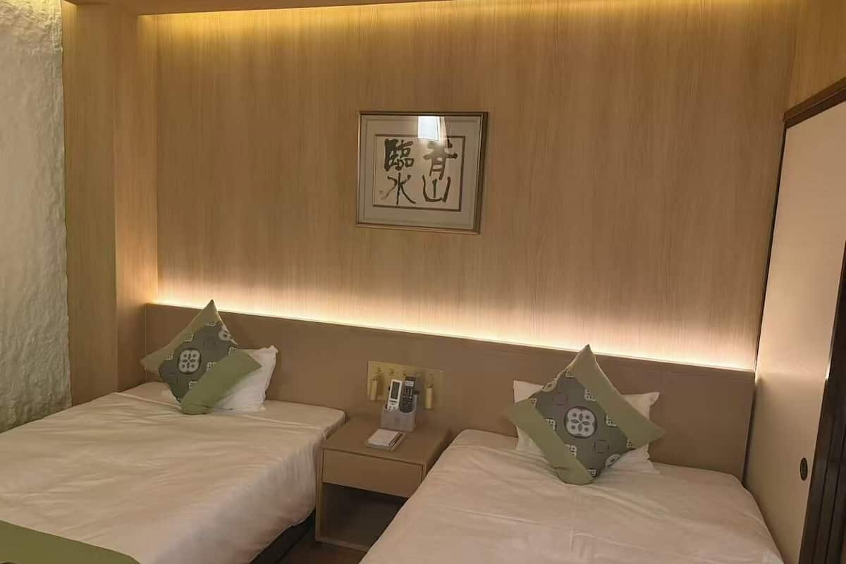A hotel room with two beds, a bedside table with a phone and a lamp, and a framed picture on the wall.