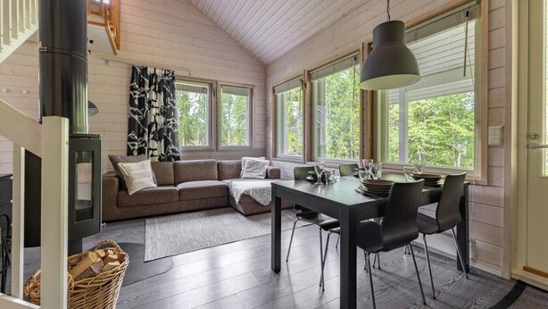 Un intérieur chaleureux avec un plafond en bois, un canapé, une table à manger avec des chaises et de grandes fenêtres.
