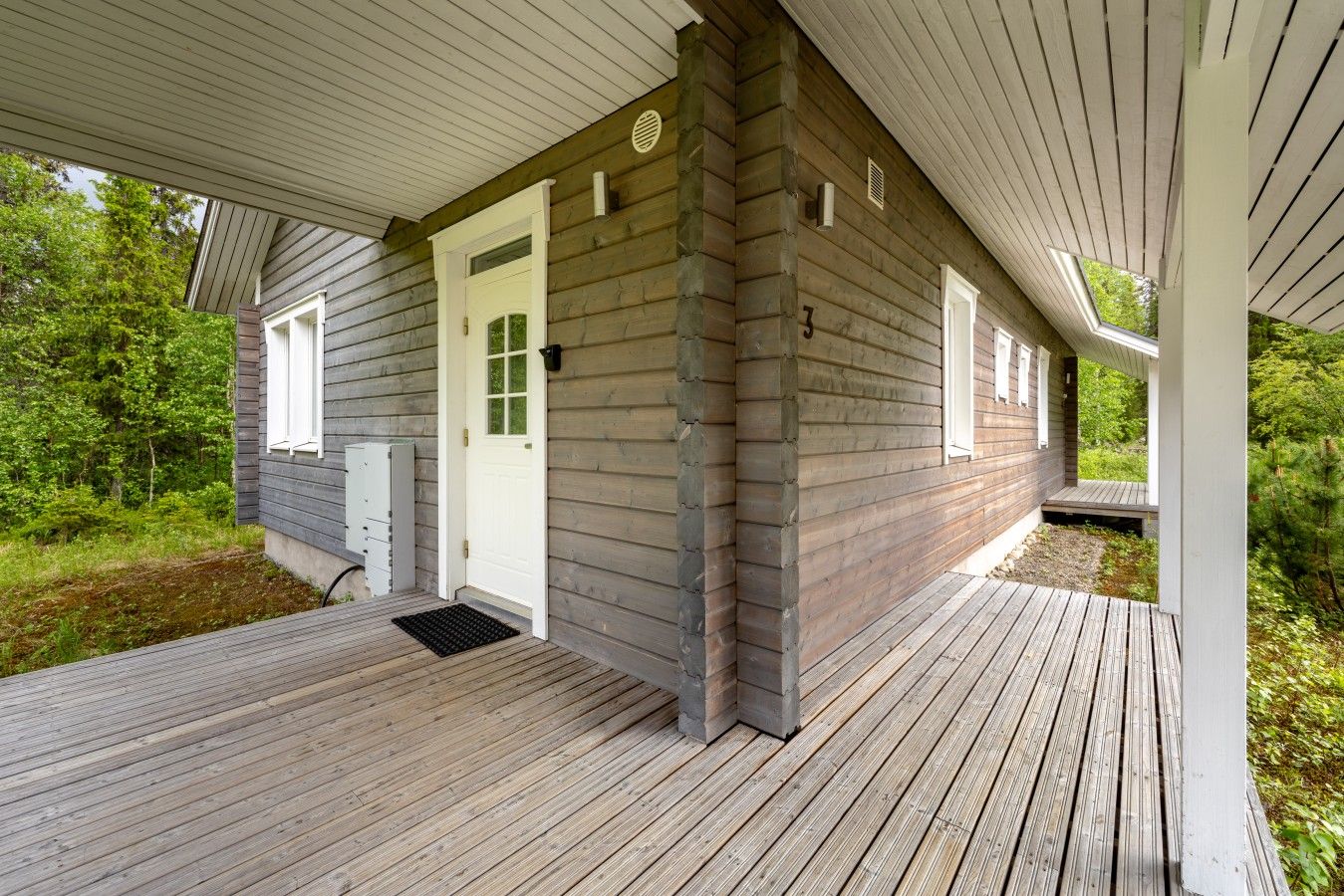 A wooden cabin with a covered porch, a white door, and a small window.