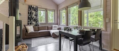 A cozy interior with a wooden ceiling, a sofa, a dining table with chairs, and large windows.