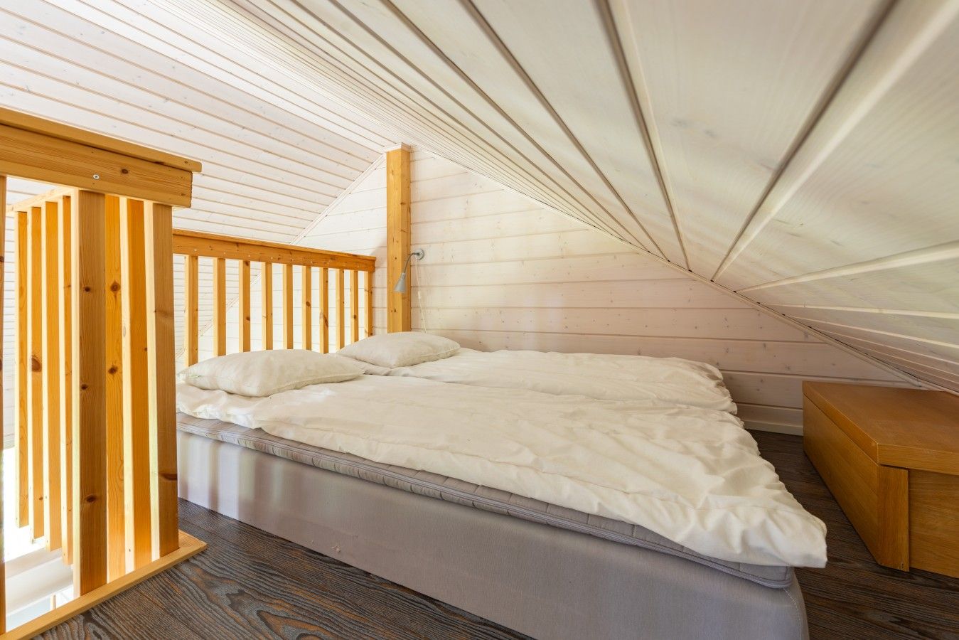 Ein Schlafzimmer mit schrägem Dach, einem Holzbettgestell, einer Matratze, einem Nachttisch und einer Lampe.