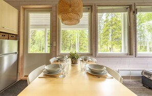 Uma sala de jantar com uma mesa de madeira posta para quatro pessoas, janelas amplas e um pendente de luz trançada.