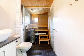 Une salle de bain avec un plafond en bois, un lavabo blanc, des toilettes et un espace douche.