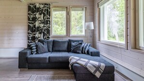 Une pièce chaleureuse avec un canapé d’angle gris, un plaid à motifs et une lampe sur pied.