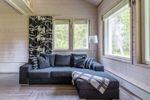 A cozy room with a grey sectional sofa, a patterned throw blanket, and a floor lamp. - Villa Lumi 1 | Cozy Arctic Retreat in Ylläs (Ylläsjärvi)