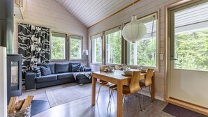 Une pièce chaleureuse avec un plafond en bois, une table à manger avec des chaises, un canapé et de grandes fenêtres donnant sur un paysage verdoyant.