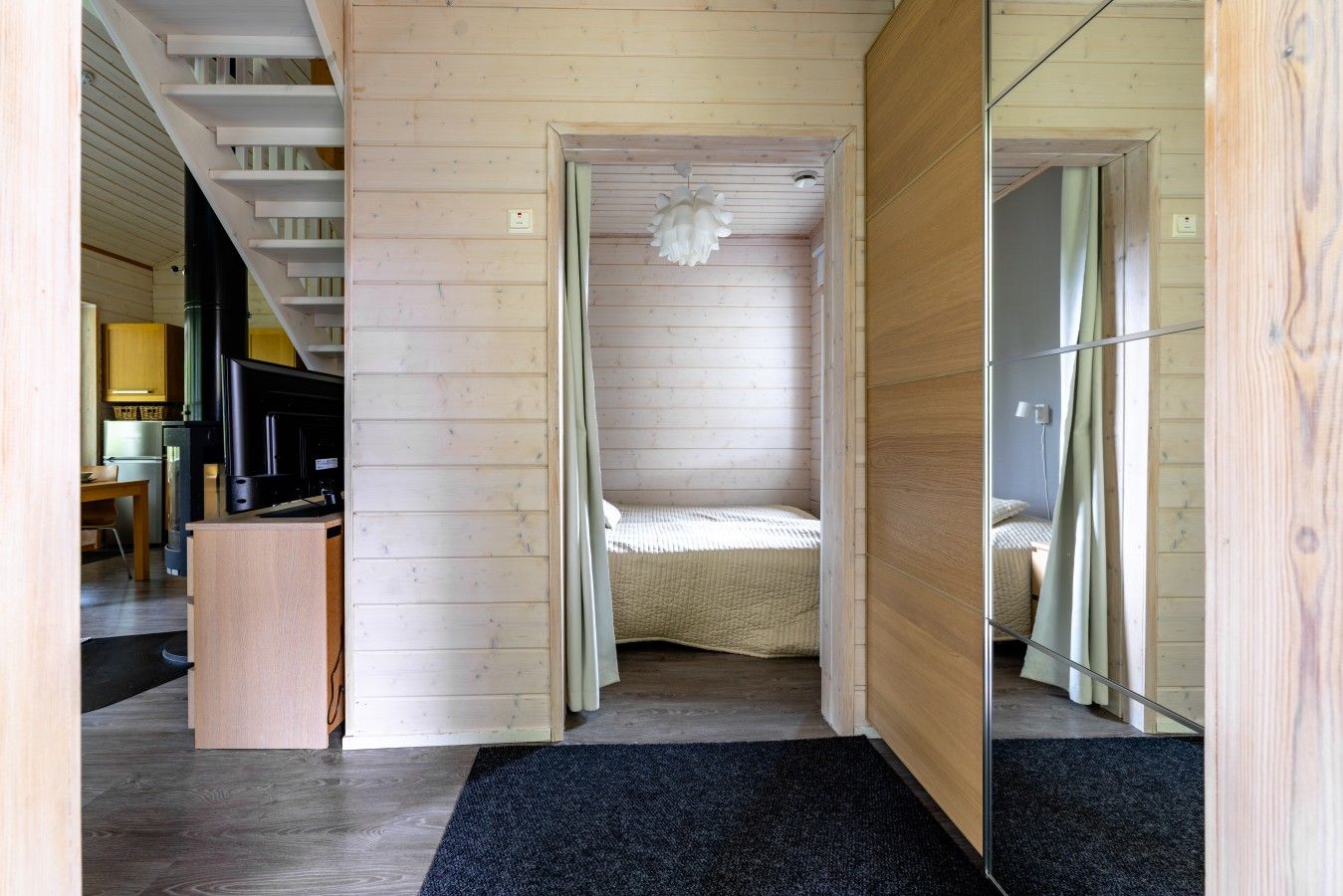 Ein schmaler Flur mit einem Bett am Ende, einem Schreibtisch mit Computer und einem Spiegel auf der rechten Seite.