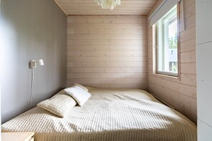 A small, cozy bedroom with a bed, a nightstand, a wall-mounted lamp, and a window. - Villa Lumi 1 | Cozy Arctic Retreat in Ylläs (Ylläsjärvi)