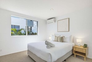 Una habitación de hotel moderna con una cama grande, una mesita de noche con lámpara y una ventana con vistas a zonas verdes.