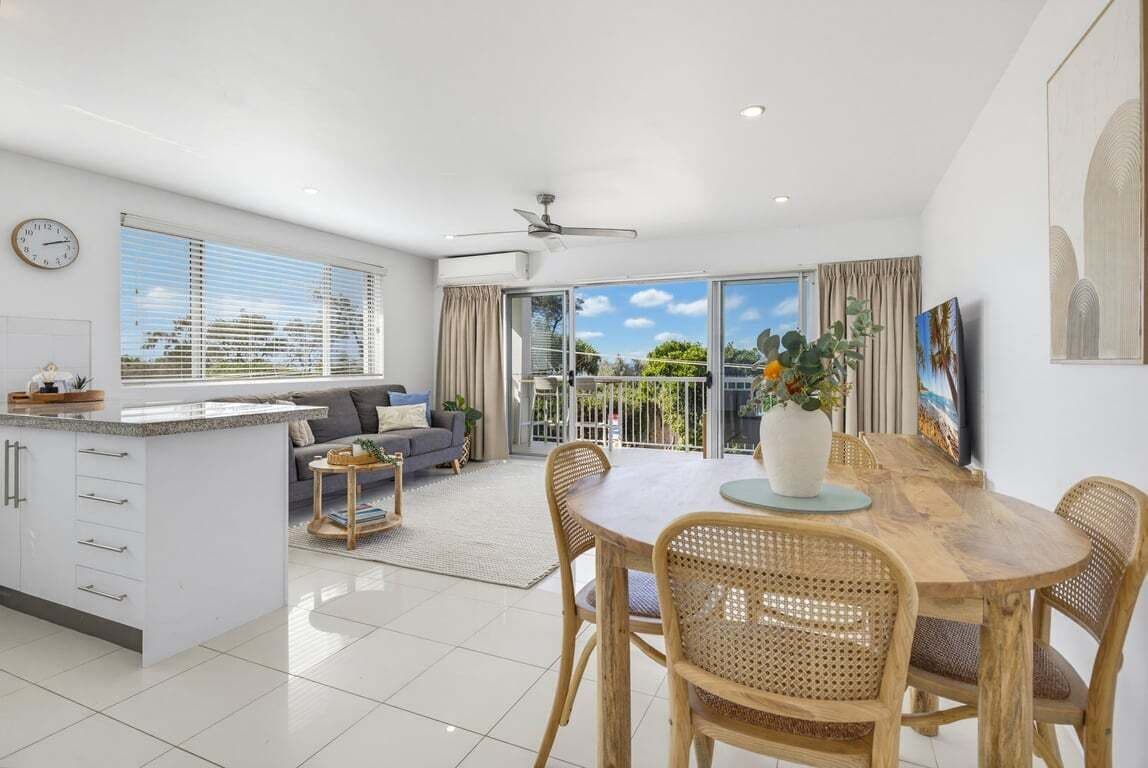 A modern kitchen with a dining area, a sofa, and a view of the outdoors.