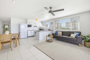 A modern kitchen with white cabinets, a central island, and a dining area with a table and chairs. - 11 Muroy Court - 50 Alexandra Parade Maroochydore (Maroochydore)