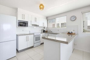 Eine moderne Küche mit weißen Schränken, einer eingebauten Mikrowelle, einem Backofen und einer Kücheninsel mit Granitplatte.