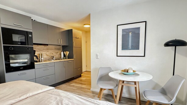 Ein modernes Hotelzimmer mit Küchenzeile, einem Bett, einem Esstisch mit Stühlen und einem gerahmten Bild an der Wand.