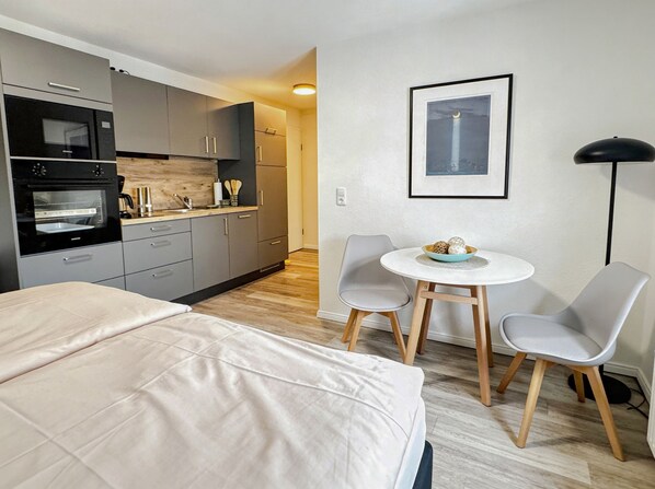 Une chambre dâhĂŽtel moderne Ă©quipĂ©e dâune kitchenette, dâun lit, dâune table Ă manger avec des chaises et dâun tableau encadrĂ© au mur.