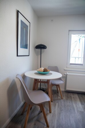 Un coin repas avec une table ronde, deux chaises, un tableau encadrĂ© au mur, un lampadaire et une fenĂȘtre donnant sur un paysage.