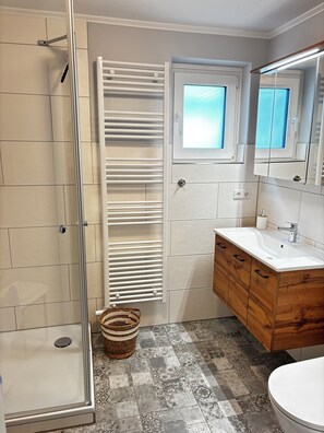 A bathroom with a shower, a sink, a mirror, and a patterned floor.