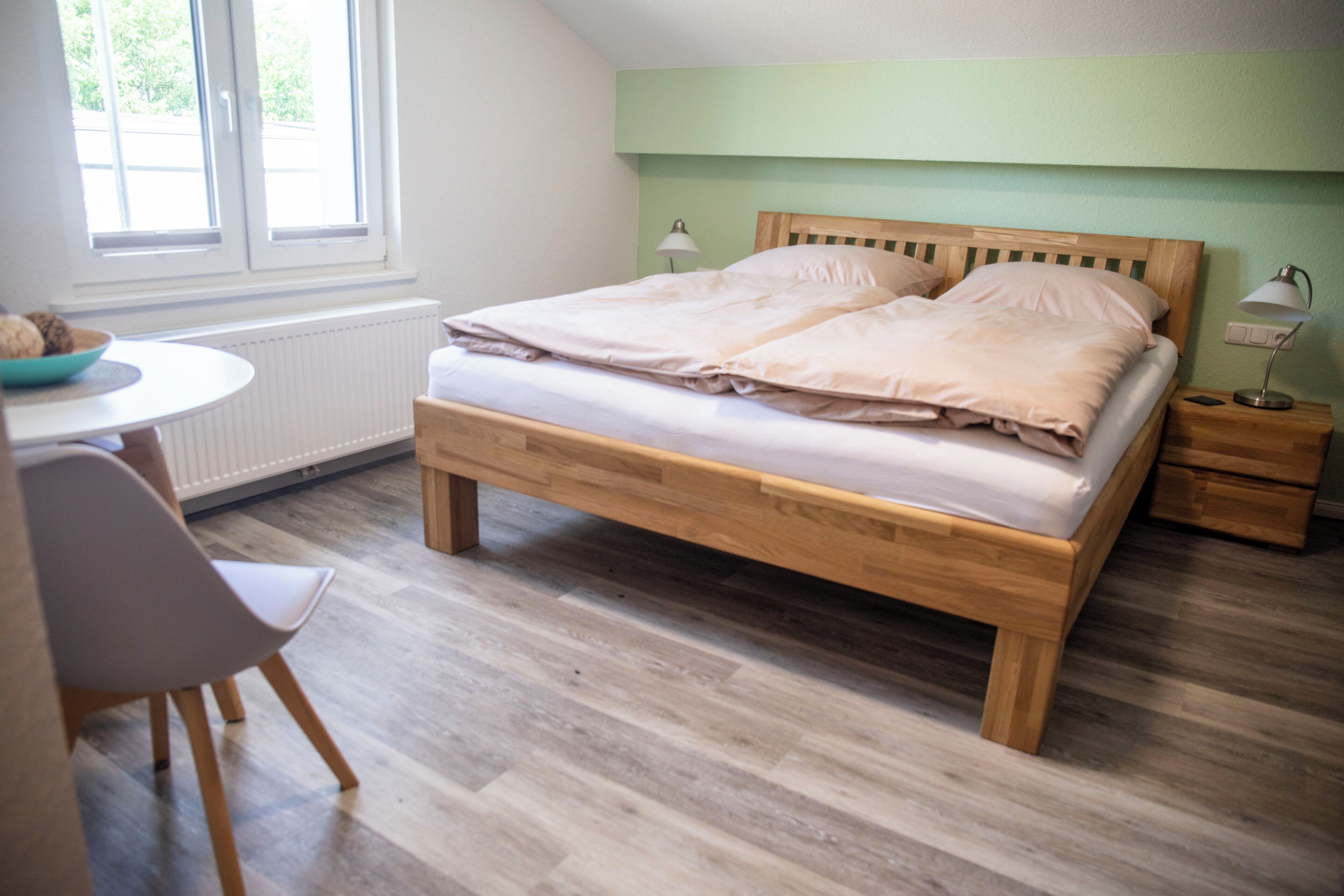 Un dormitorio con una cama de madera, mesitas de noche, una silla y una ventana.