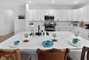 A modern kitchen with white cabinets, a central island, and a dining area with chairs.