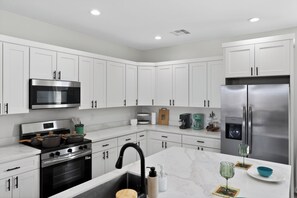 A modern kitchen with white cabinets, stainless steel appliances, and a marble countertop.