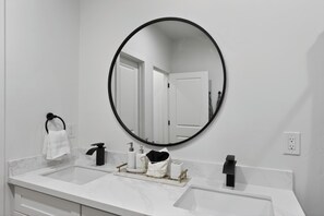 A bathroom with a white marble countertop, a black faucet, a round mirror, and a towel rack.