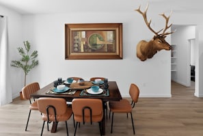 A dining area with a wooden table, orange chairs, and a mounted deer head.