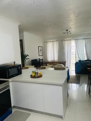 Eine moderne Küche mit Kochinsel, ein Essbereich mit blauem Sofa und ein Wohnzimmer mit Fernseher.