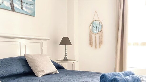 A neatly made bed with blue towels, a bedside lamp, and a wall decoration. - Casa Amadeus Corralejo (Corralejo)