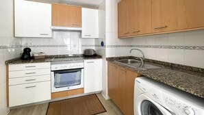 A compact kitchen with white cabinets, a built-in oven, a washing machine, and a sink. - Casa Amadeus Corralejo (Corralejo)