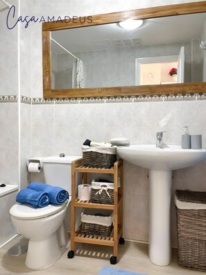 Een badkamer met toilet, wastafel, spiegel en een houten plank met manden en handdoeken.