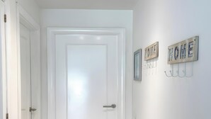 A hallway with a white door, wooden flooring, and wall-mounted hooks with 'HOME' signs. - Casa Amadeus Corralejo (Corralejo)