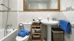 A bathroom with a toilet, sink, and shower. There are towels and baskets on the shelves. - Casa Amadeus Corralejo (Corralejo)
