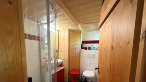 Une salle de bain avec une douche à parois de verre, des toilettes rouges et un lavabo blanc.