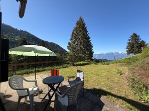 An outdoor seating area with a table and chairs, a green umbrella, and a mountain view. - Chalet 1813 Nature & Panorama (Montreux)