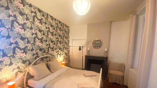 A bedroom with a bed, bedside lamps, a fireplace, and a wall with a floral pattern.