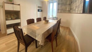 A dining area with a table covered in plastic, surrounded by wooden chairs, a microwave above the table, and a patterned wall.
