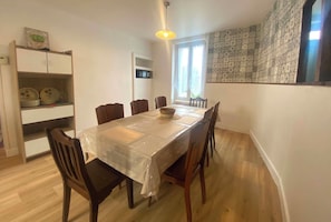 Un comedor con una mesa cubierta con plástico, rodeada de sillas de madera, un microondas encima de la mesa y una pared con diseño.