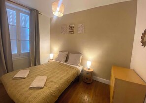 A bedroom with a bed, bedside lamps, a nightstand, a window with curtains, and wall art.