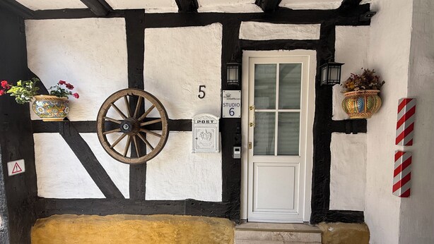 A traditional building facade with a white door, a number '5' sign, a post box, and a wheel.