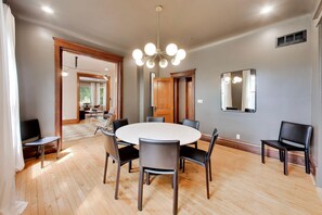 Un comedor con una mesa redonda y sillas, una araña y un espejo grande en la pared.
