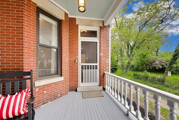 A porch with a white railing, a bench with red and white cushions, and a door with a glass panel.